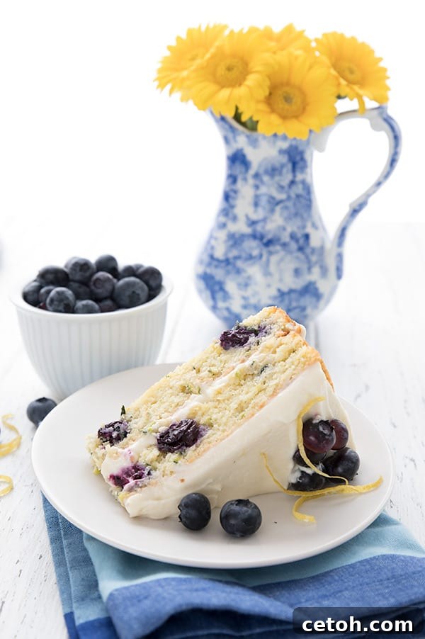 A slice of lemon blueberry zucchini later cake on a white plate with a vase of yellow flowers in the background.