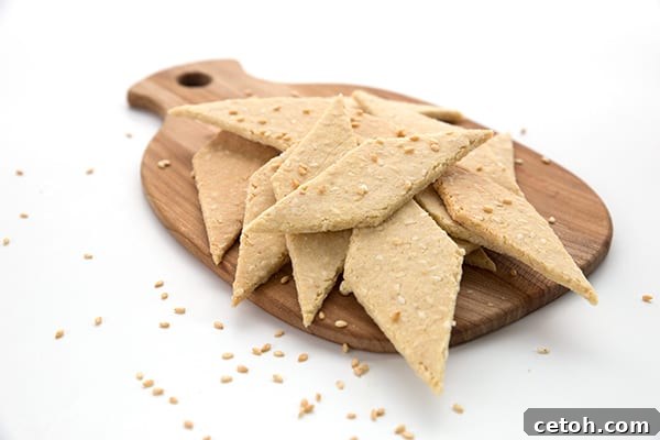 Keto sesame crackers in a pile on a wooden cutting board