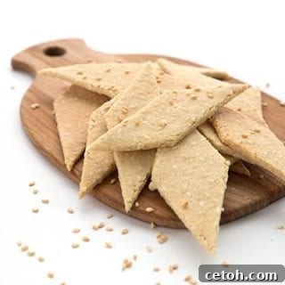 Keto sesame crackers in a pile on a wooden cutting board