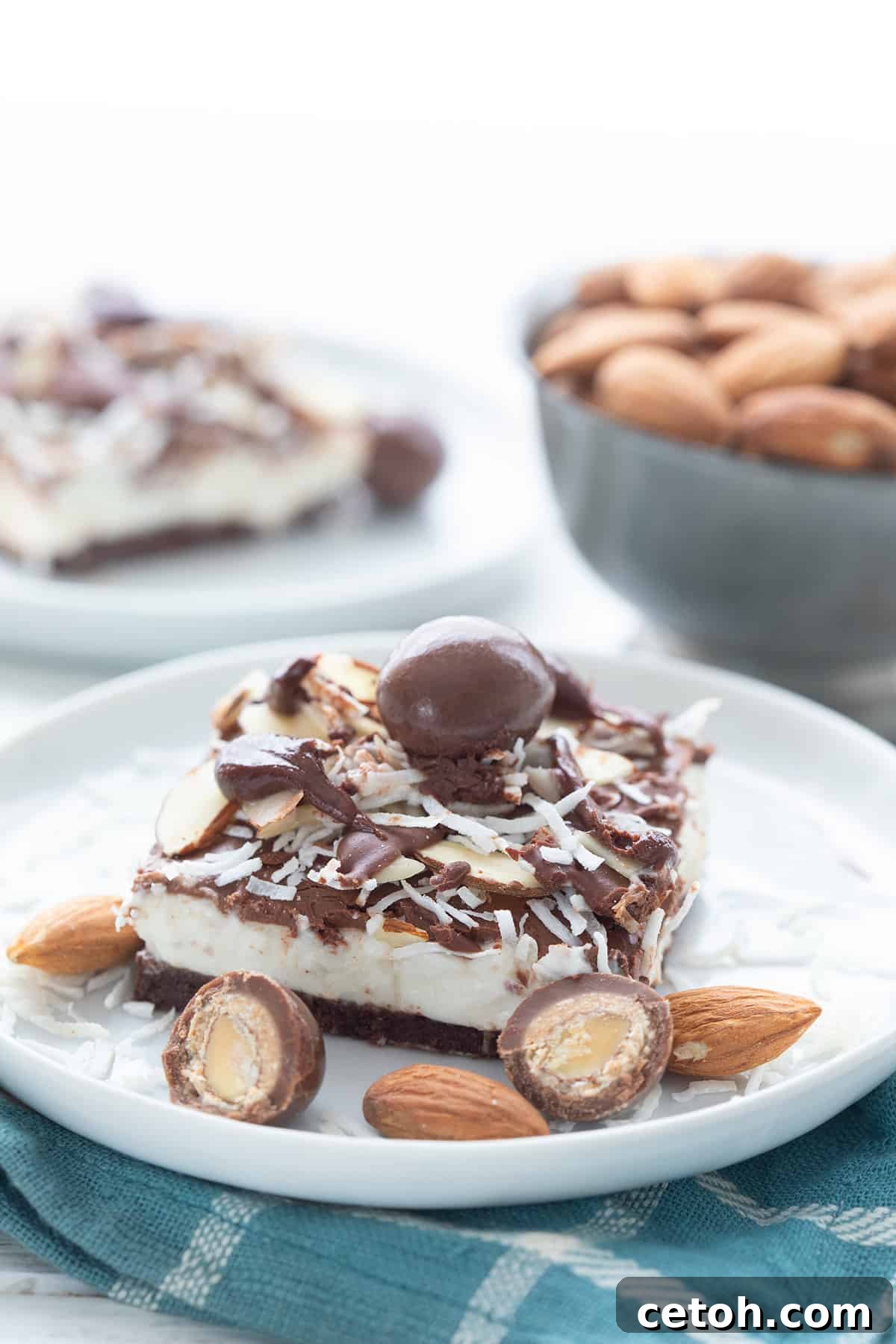 A keto no bake cheesecake bar on a white plate, over a teal napkin, with sugar-free chocolate covered almonds around it.