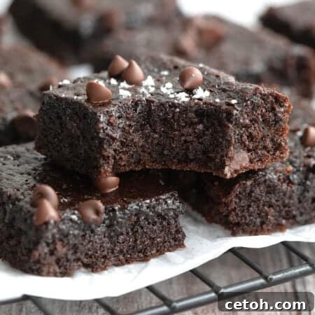 Fudgy keto brownies piled up on a baking rack with a bite taken out of the top one.
