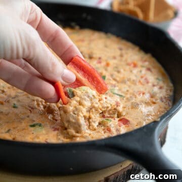 A hand dipping a vibrant red bell pepper slice into the rich, cheesy Sausage Cheese Dip.