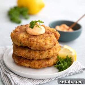 A stack of 3 perfectly cooked keto crab cakes on a white plate, topped with a dollop of spicy mayo for an appetizing finish.
