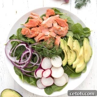 A large platter of spinach salad with salmon and avocado