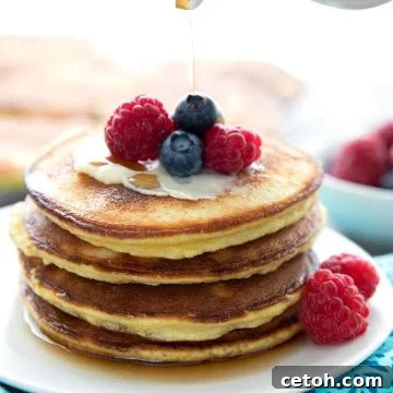A stack of keto coconut flour pancakes on a white plate, with berries on top.
