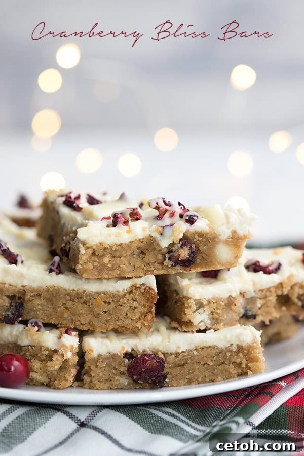 Keto copycat cranberry bliss bars on a white plate, bathed in the soft glow of Christmas lights in the background.