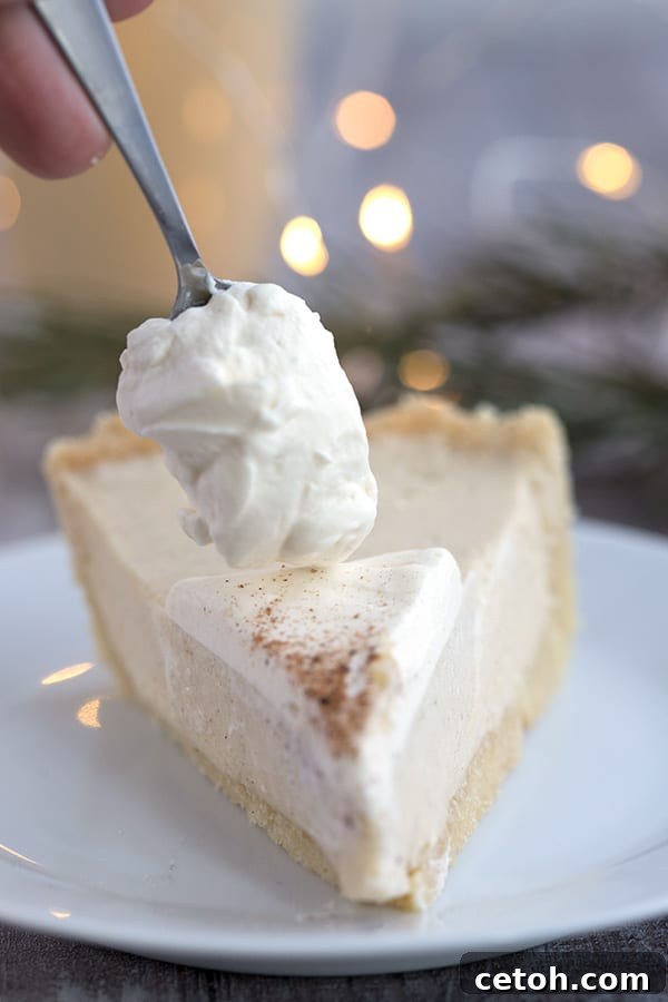 Whipped cream being dolloped generously over a freshly cut piece of keto eggnog pie, ready to be served.