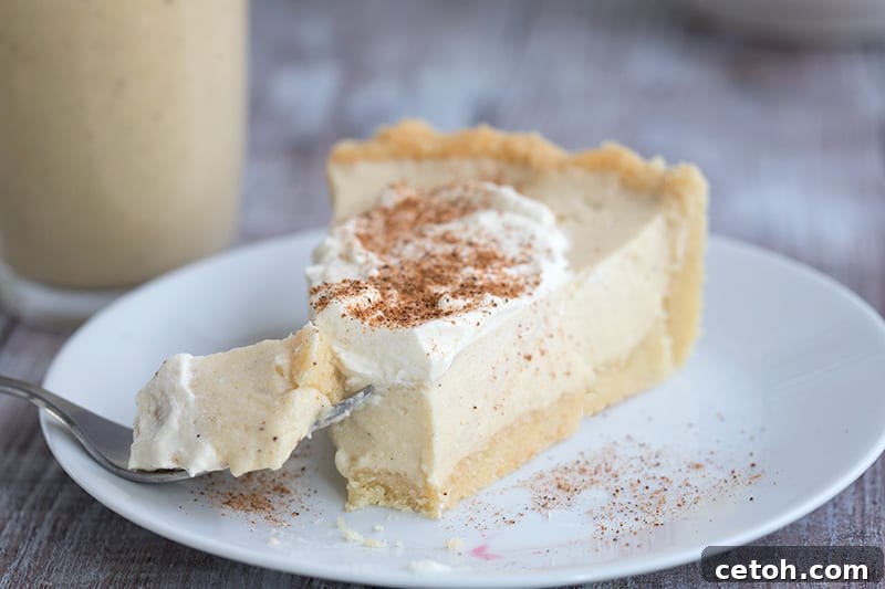 A beautifully presented slice of keto eggnog pie on a white plate, topped with a dollop of whipped cream and a sprinkle of fresh nutmeg. 