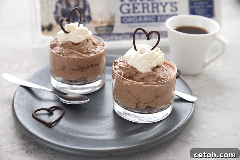 Two dessert cups with no bake French silk pie on a dark blue plate with a carton of eggs in the background. 
