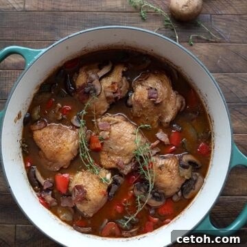 Top down image of Keto Coq au Vin in a teal dutch oven on a wooden table, with mushrooms and sprigs of thyme.