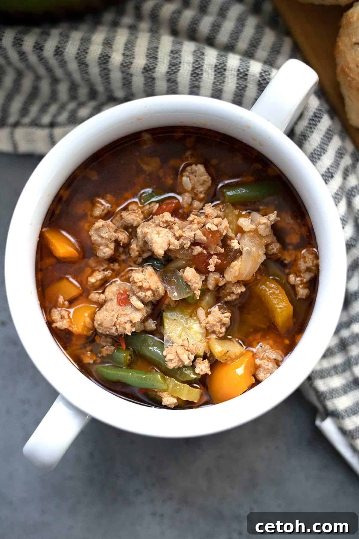 An inviting top-down image of keto Italian sausage soup served in a white bowl with elegant handles.