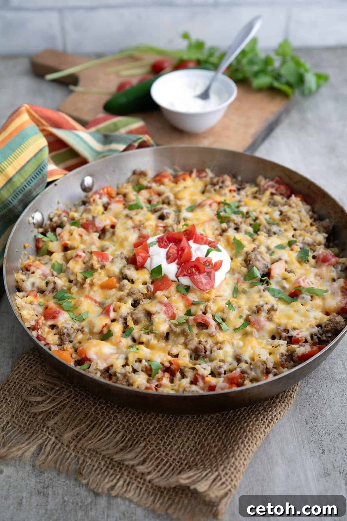 Mexican Cauliflower Rice in a skillet with sour cream, cilantro, and chopped tomatoes on top.