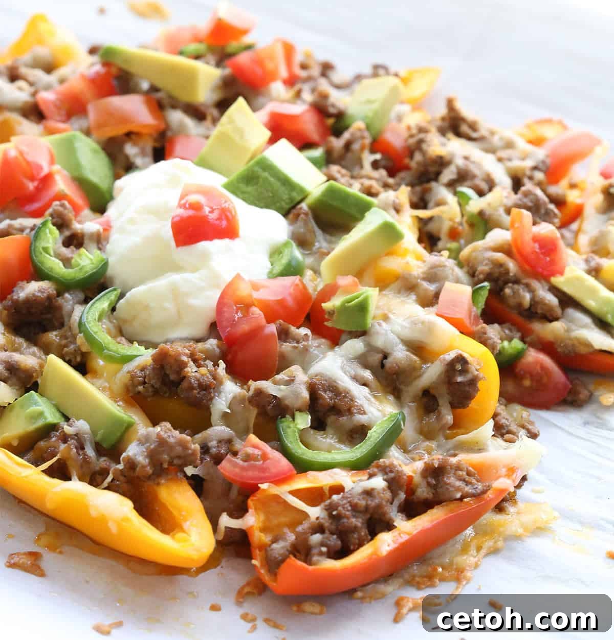 Mini Pepper Keto Nachos on a piece of white parchment paper, with sour cream on top.