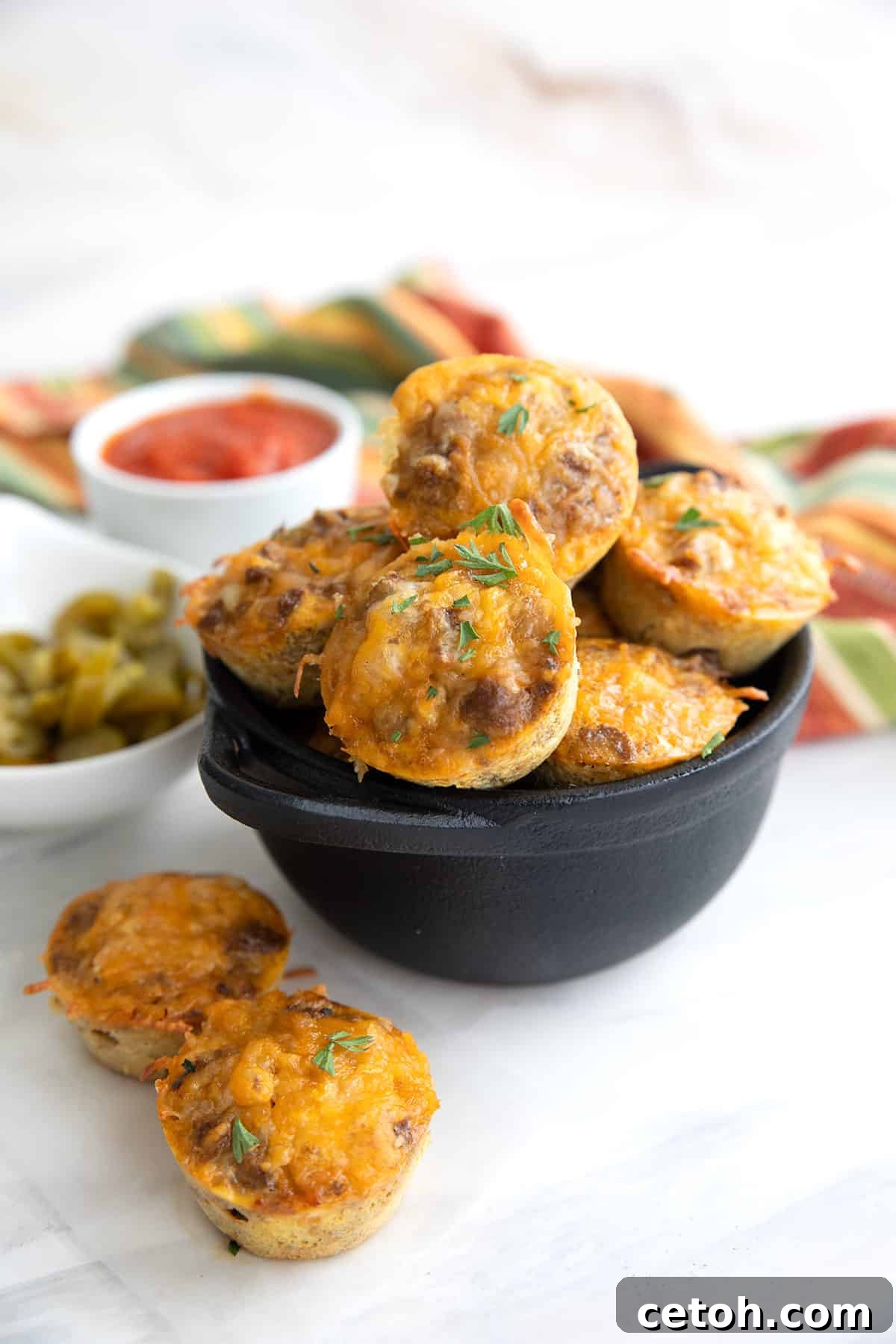Keto Taco Bites piled up in a black cast iron dish, with two sitting in front.