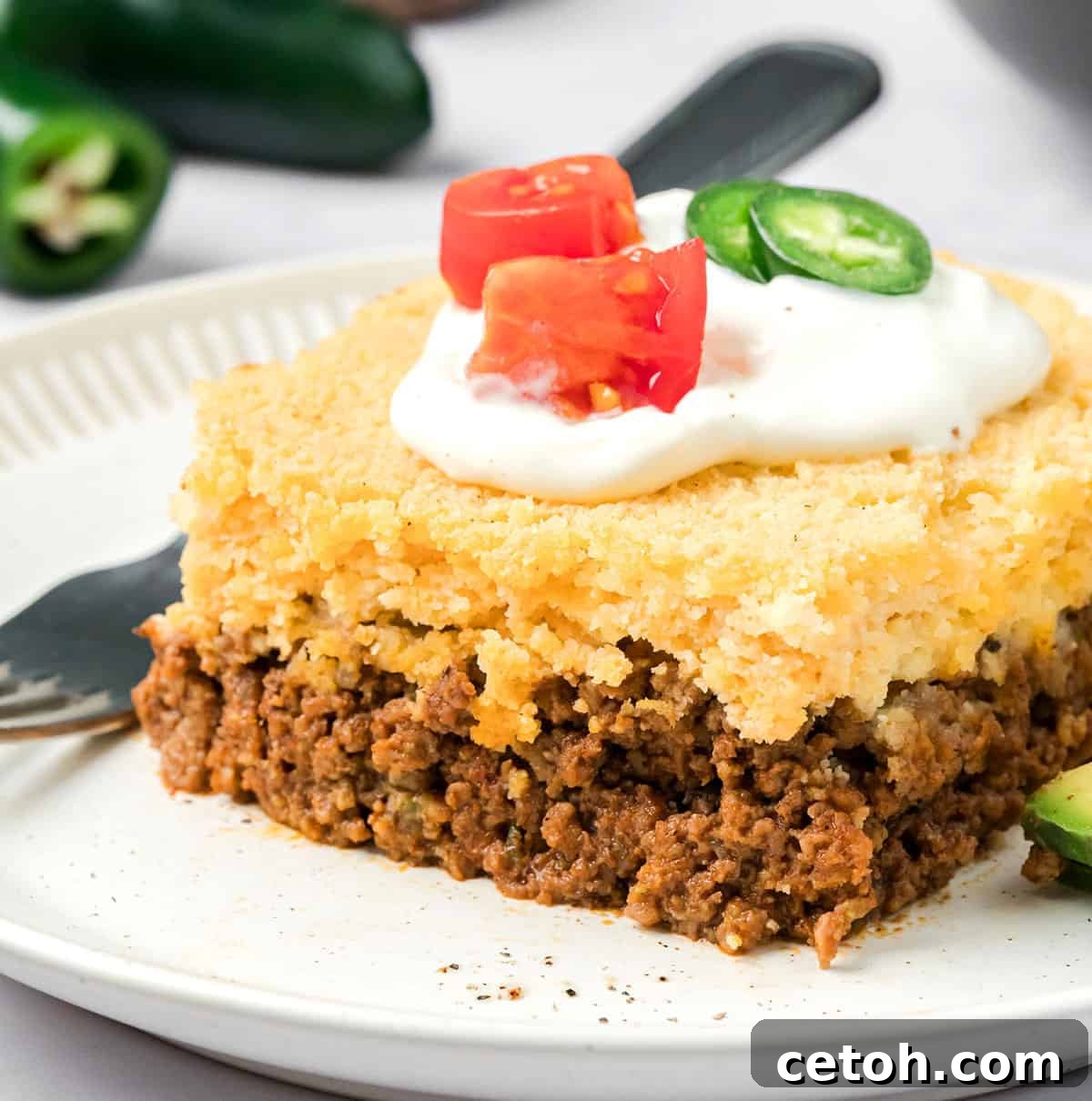 Close up shot of a serving of Keto Tamale Pie on a white plate with sour cream and chopped tomatoes on top.