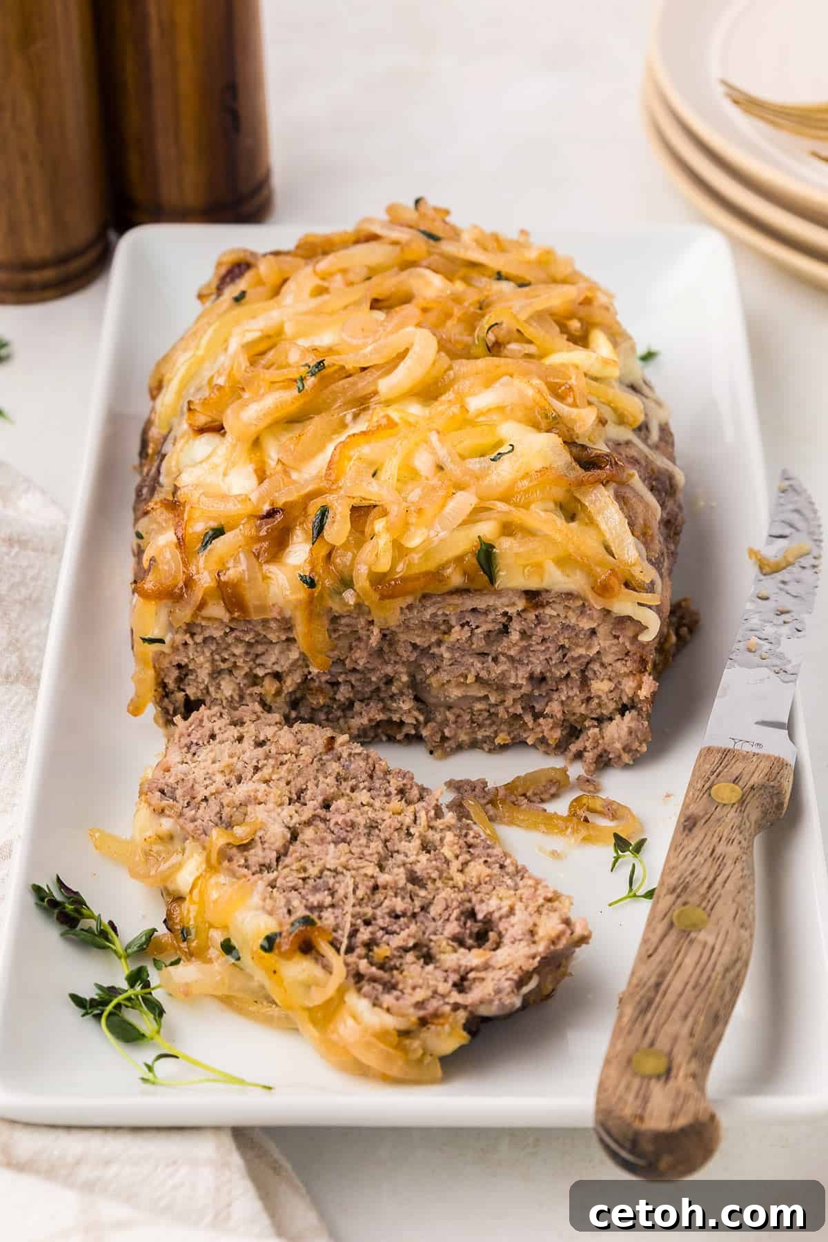 French Onion Meatloaf on a white platter with a knife, with one slice cut out.