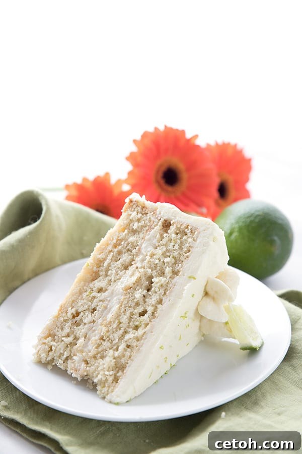 Keto Tequila Lime Delight 4 A slice of keto margarita cake on a white plate with limes and gerbera daisies in the background.