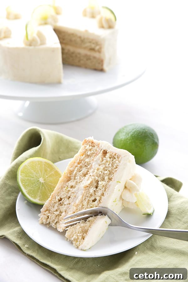 Keto Tequila Lime Delight 5 A slice of margarita cake on a white plate over a green napkin, with limes and the rest of the cake in the background.
