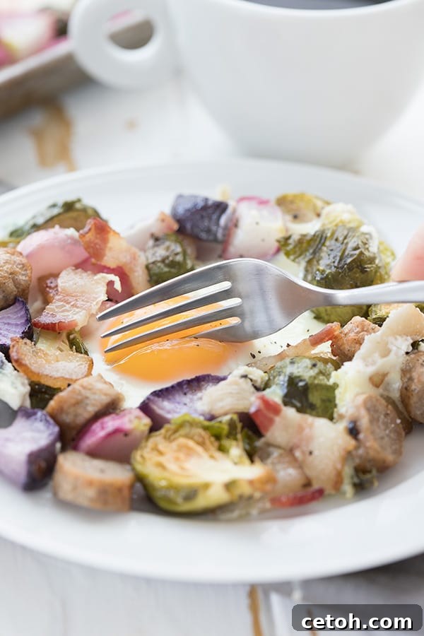 Sheet Pan Keto Morning Delight 5 A fork digging into a runny egg on a plate filled with vegetables and sausage