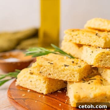 A plate of Keto Focaccia Bread sits in front of a bottle of olive oil, highlighting its delicious appearance.