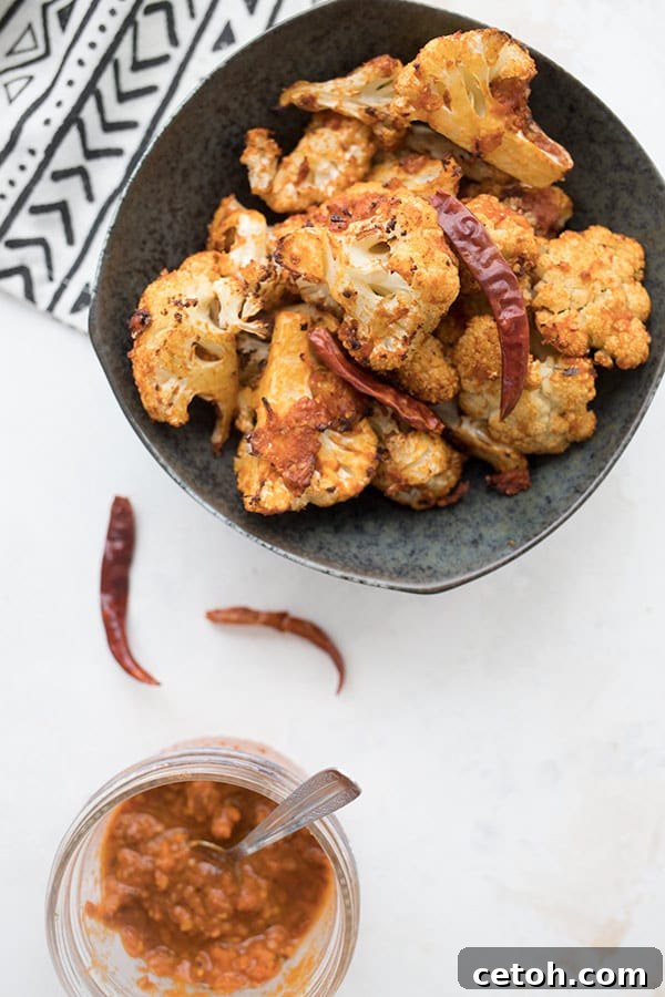 Top-down photo of a bowl of perfectly cooked air fryer cauliflower, prominently featuring a jar of homemade harissa chili paste in the foreground.