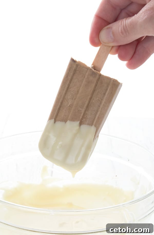 Frozen Keto Coffee Delights 3 A creamy coffee popsicle being carefully dipped into a bowl of melted sugar-free white chocolate, creating a delicate coating.