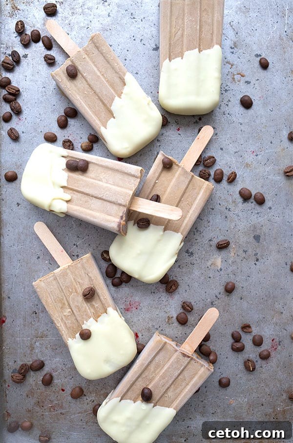 Frozen Keto Coffee Delights 4 Top-down photo of white chocolate-dipped keto coffee popsicles arranged neatly on a white surface, with whole coffee beans scattered artistically around them.