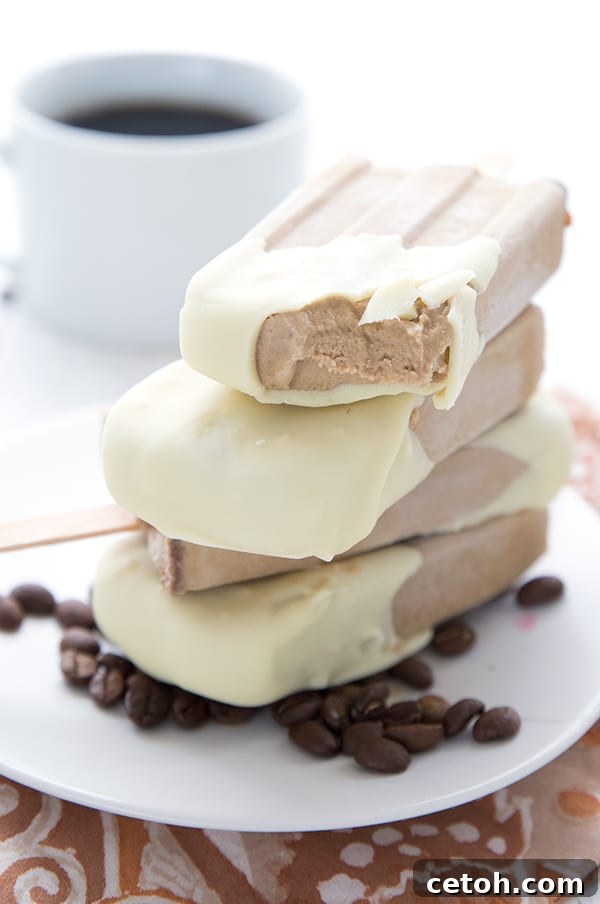 Frozen Keto Coffee Delights 5 Close-up shot of stacked keto coffee popsicles on a white plate, garnished with coffee beans. One popsicle has a bite taken out, revealing its creamy interior.