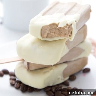 Close up shot of keto coffee popsicles stacked on a white plate with coffee beans. A bite has been taken out of one popsicle