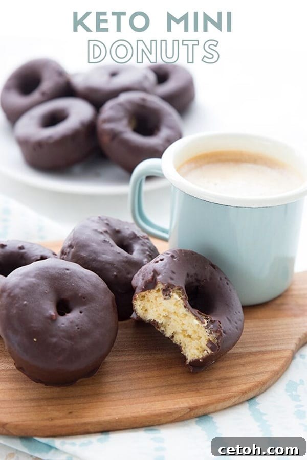 Irresistible Keto Chocolate Minis 2 A small cutting board with a cup of coffee and some chocolate covered mini donuts. A bite is taken out of the front donut. There is a white plate in the background with more donuts.