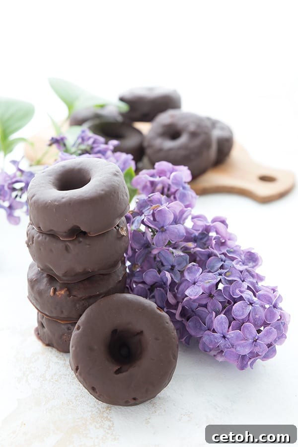Irresistible Keto Chocolate Minis 3 A stack of keto mini donuts with a sprig of lilacs. A cutting board in the background with more donuts on it.