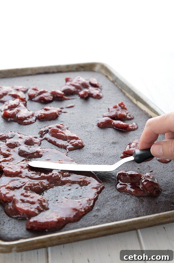 Close-up shot of a rich cherry filling being spread meticulously over the dark chocolate sponge of a Keto Black Forest sheet cake, showcasing the vibrant red fruit layer.