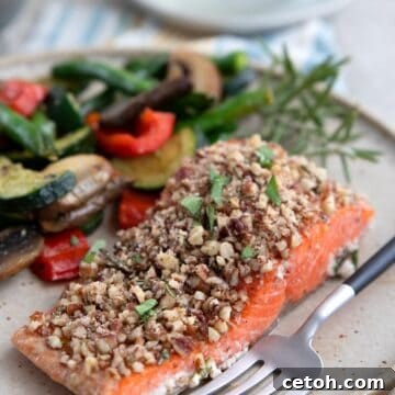 A serving of Pecan Crusted Salmon on a plate with sautéed veggies.