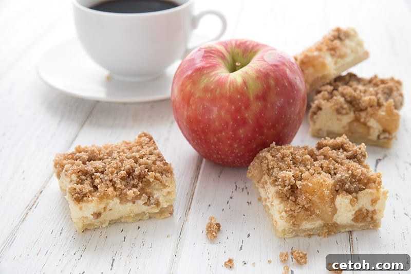 Keto Apple Pie Cheesecake Bars on a white wooden table with an apple and a cup of coffee