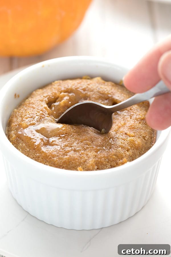 A spoon digging into a keto pumpkin lava cake on a white plate, revealing the warm, flowing caramel interior.