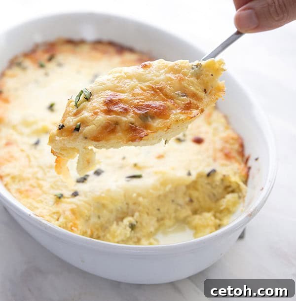 A generous serving of creamy spaghetti squash casserole being scooped out of a white baking dish with a large spoon, showing its cheesy goodness.