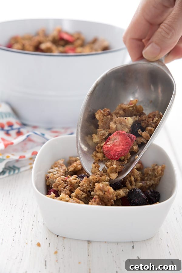 A metal scoop pouring keto granola into a white bowl.