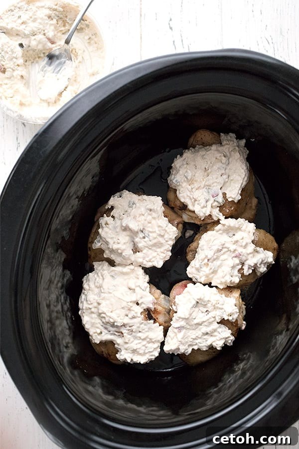 A close-up, top-down view of succulent chicken thighs simmering in a slow cooker, generously topped with creamy Queso dip, promising a rich and flavorful meal.