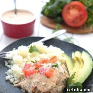 Titled image for Keto Slow Cooker Smothered Chicken, with a piece of chicken on a black plate with cauliflower rice and avocado.