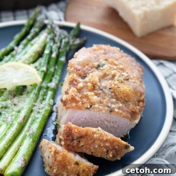 A parmesan crusted pork chop on a blue plate, with two pieces sliced off and some asparagus on the side.