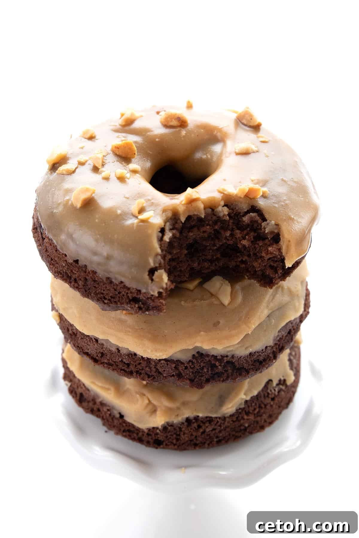 A stack of Keto Chocolate Peanut Butter Donuts on a white cupcake stand, with a bite taken out of the top one.