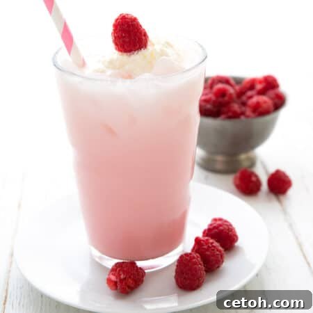 A tall glass of keto Italian Cream Soda on a white plate with fresh raspberries.