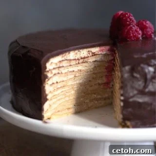 Keto crepe cake on a white cake plate with a slice cut out of it.