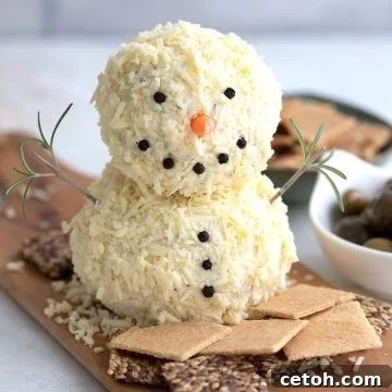 A snowman shaped cheeseball on a platter surrounded by crackers.
