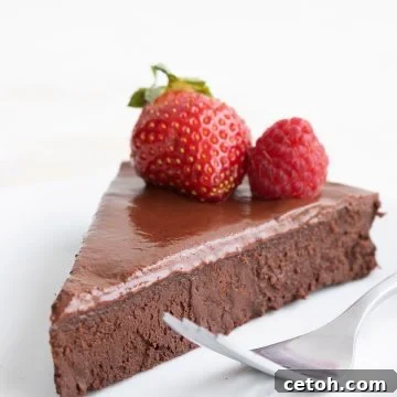 A slice of dairy-free keto flourless chocolate cake on a white plate with two berries on top.