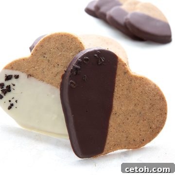 Two keto espresso shortbread cookies propped up on a white table with more cookies in the background.