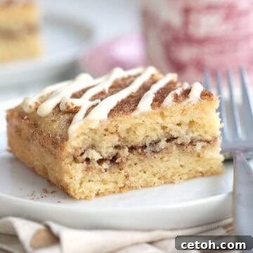 Close up shot of a slice of Keto Cinnamon Roll Coffee Cake on a white plate with a patterned red coffee cup in the background.