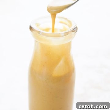 A spoon drizzling sugar free keto honey mustard into a glass bottle.