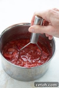 Mashing strawberries and rhubarb in a pot for sauce.