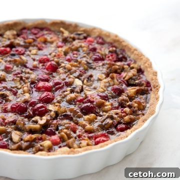 Keto Tangy Cranberry Walnut Delight 2 Freshly baked Keto Cranberry Walnut Tart in a white tart pan, ready to be served on a marble countertop.
